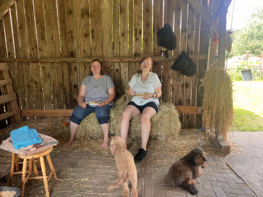 Zwei Frauen im Stall auf Heuballen sitzend und essend